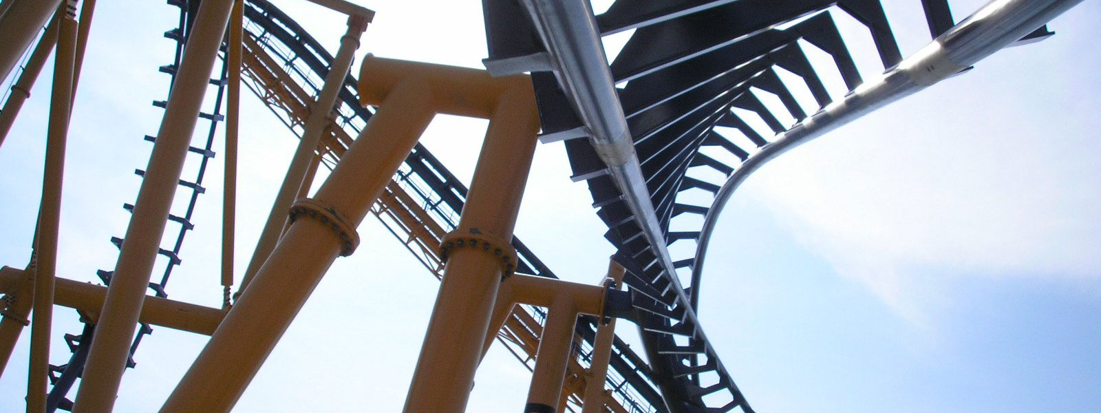 Close-up of a roller coaster track with multiple loops and turns, supported by orange pillars, set against a visible sky backdrop.