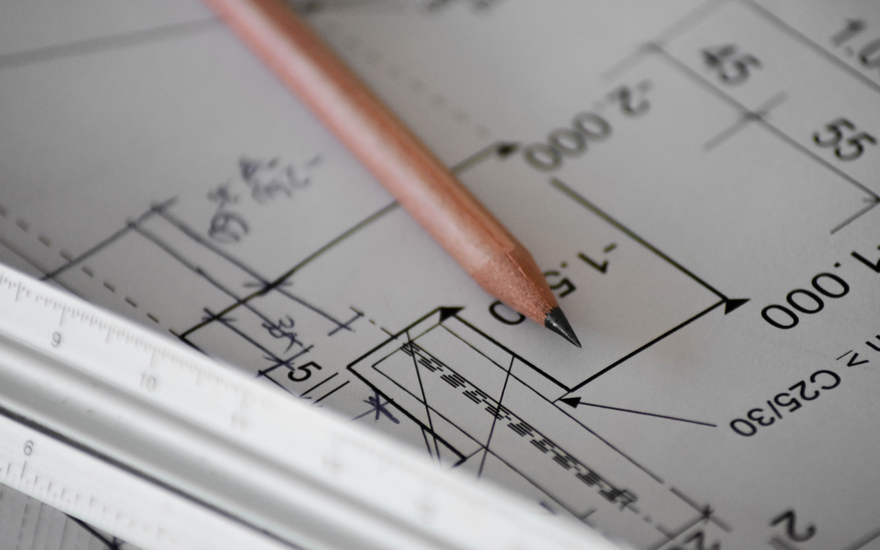 Close-up of an architectural or engineering blueprint with a pencil resting on top, showing technical drawings and measurements