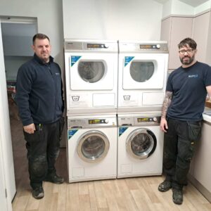 Two WASHCO installers standing next to newly installed washers and dryers in a Young Lives vs Cancer house