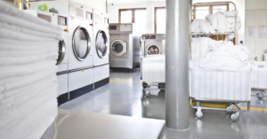 image of a clean hospital laundry room with commercial washing machines and dryers and white linens on a table and in laundry carts.